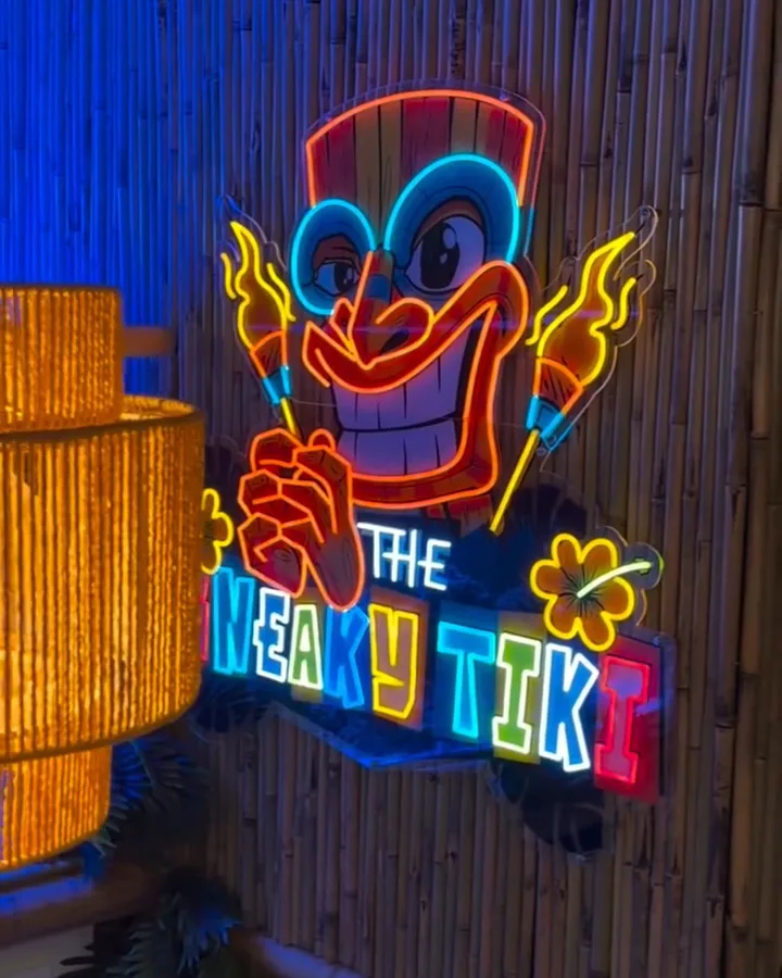A woven bamboo pendant lamp beside the neon tiki sign